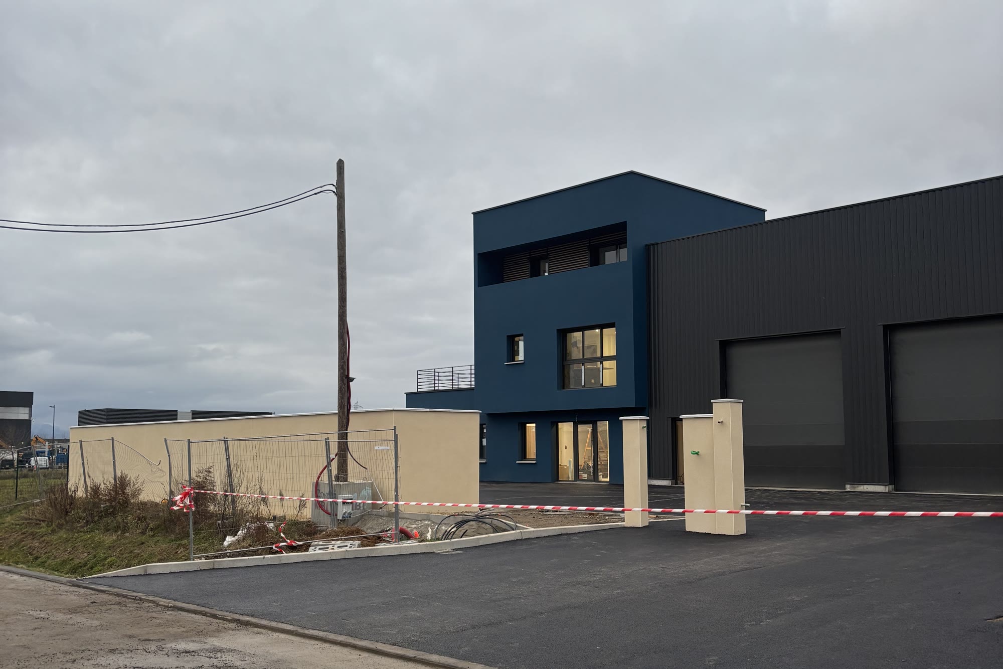 Bâtiment tertiaire et hangar terminés, façade bleue et bardage, parking bitumé — après travaux