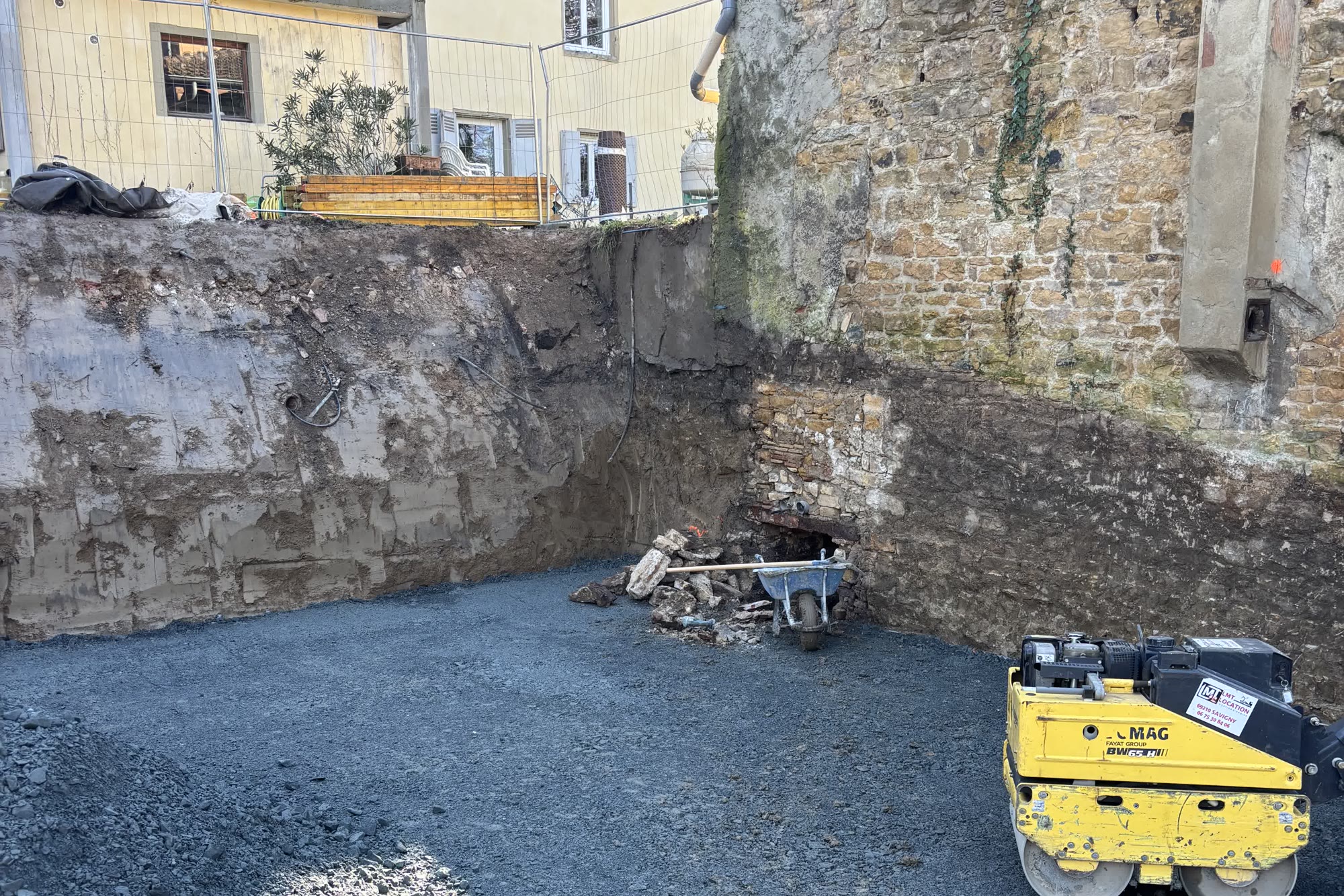 Cour en cours de terrassement : fouille et compactage entre deux bâtiments — avant travaux